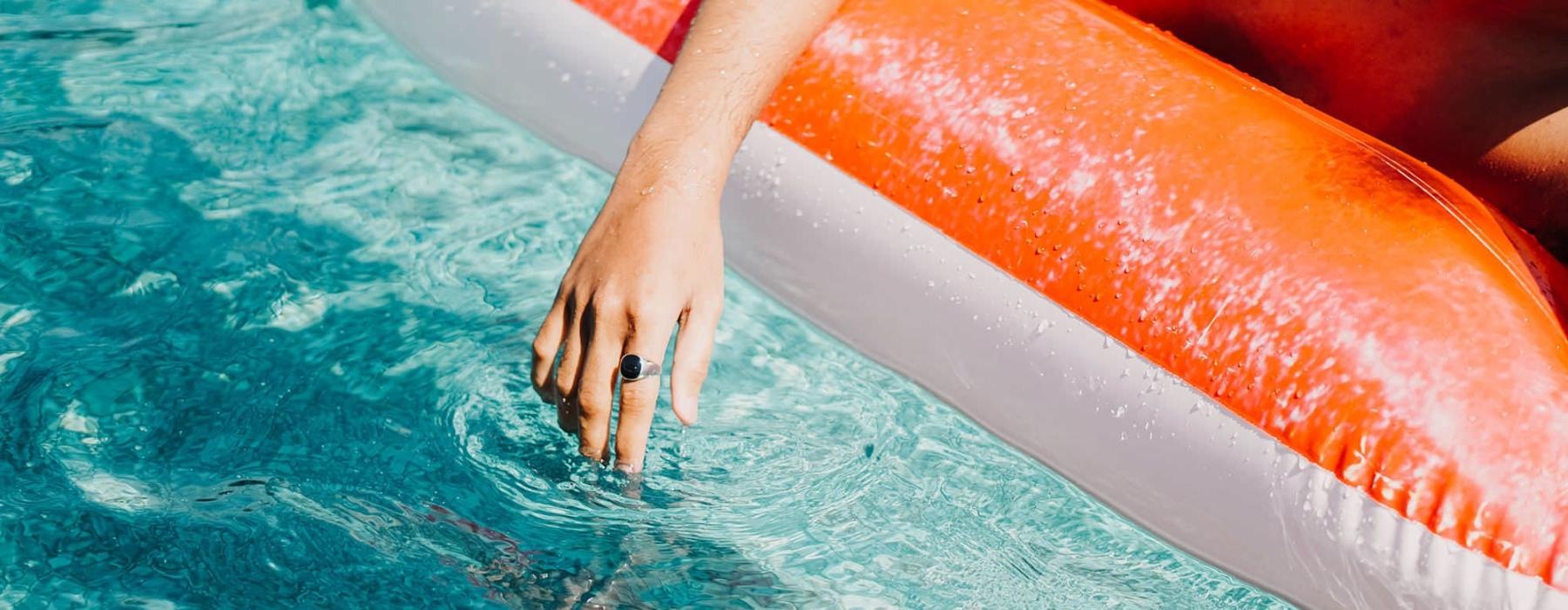 woman dangles her hand in the pool as she floats in an inflatable vessel