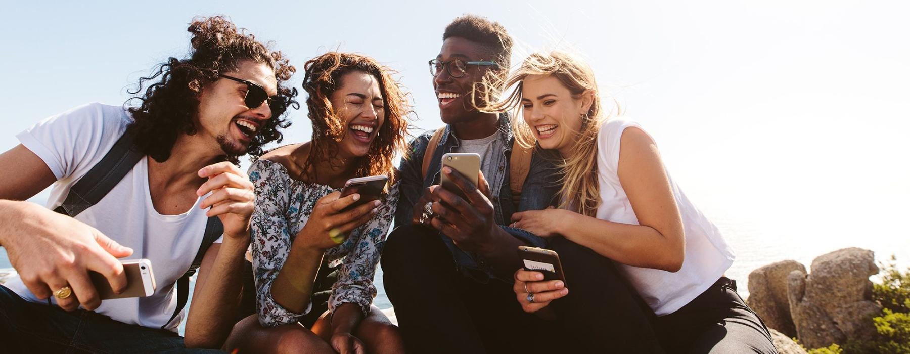 a group of friends sit outside laughing over their cell phones