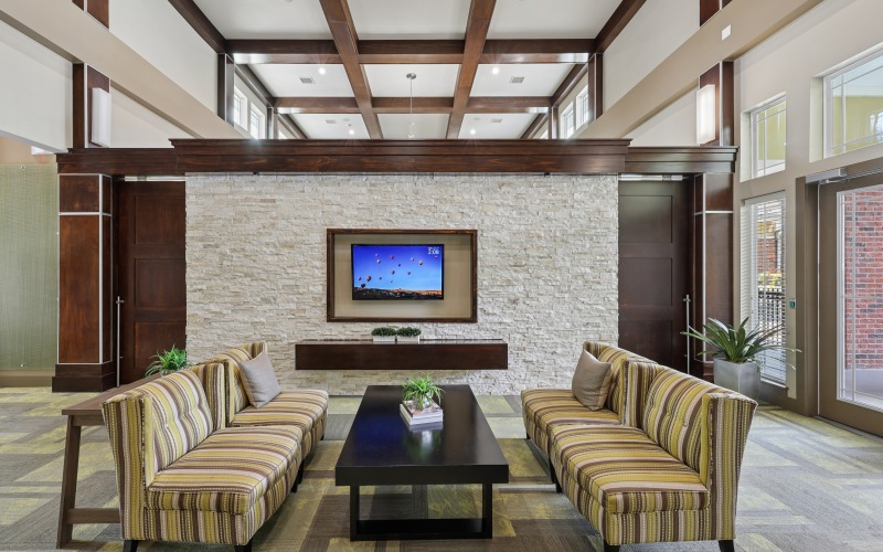 Clubhouse lounge at Stone Pointe apartments featuring striped sofas, a stone fireplace wall with a TV, and vaulted wood-beam ceilings.