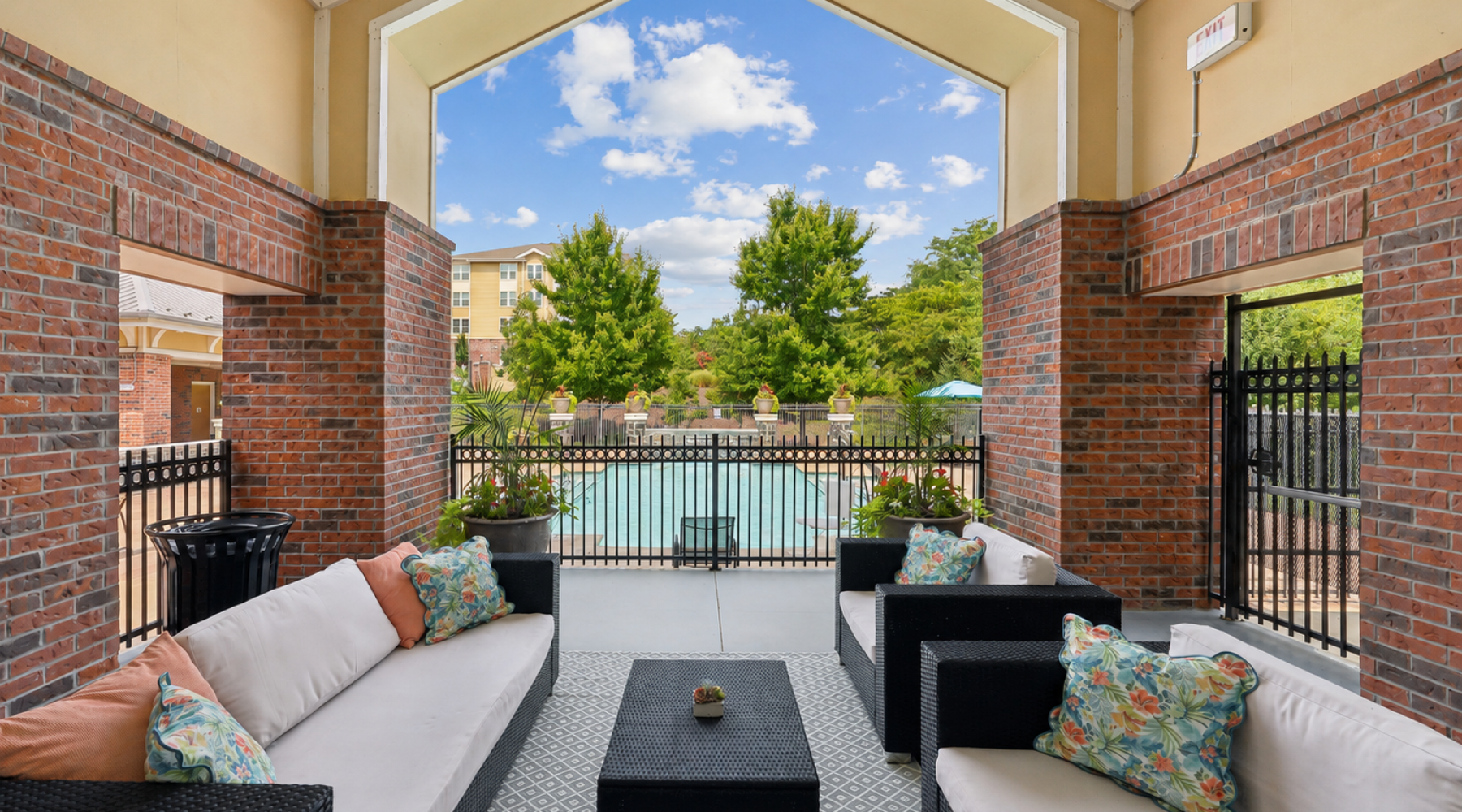Covered outdoor patio lounge at Stone Pointe apartments featuring brick arches, comfortable cushioned seating, and views of the swimming pool.