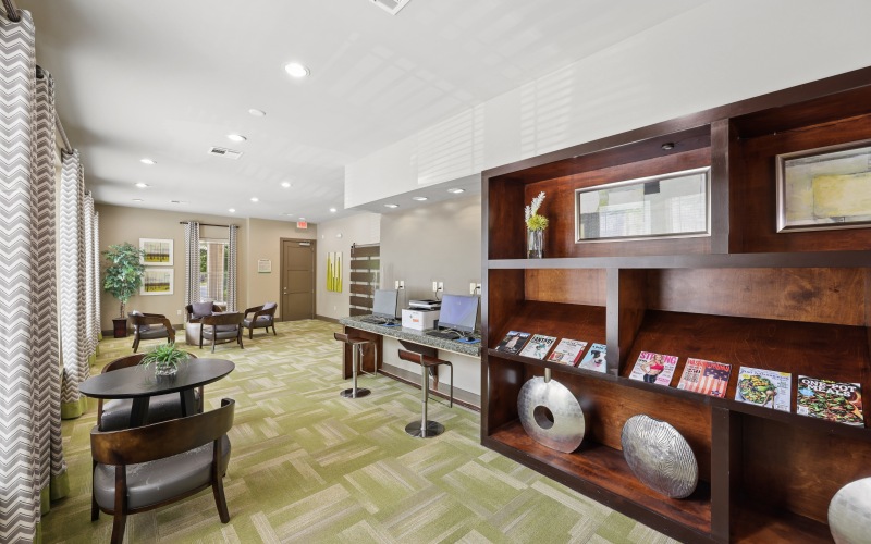 Modern business center at Stone Pointe apartments featuring computer workstations, seating, and decorative shelving with magazines