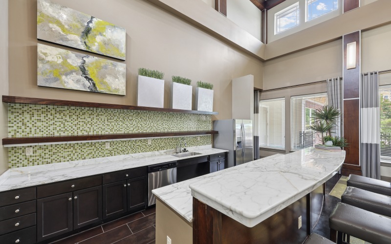 Clubhouse community kitchen and bar area at Stone Pointe apartments featuring marble countertops, dark cabinetry, and barstool seating.
