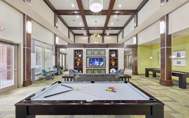 Clubhouse gathering space at Stone Pointe apartments featuring soft accent lighting, a large dining and board game table, plush seating, and warm decorative accents.
