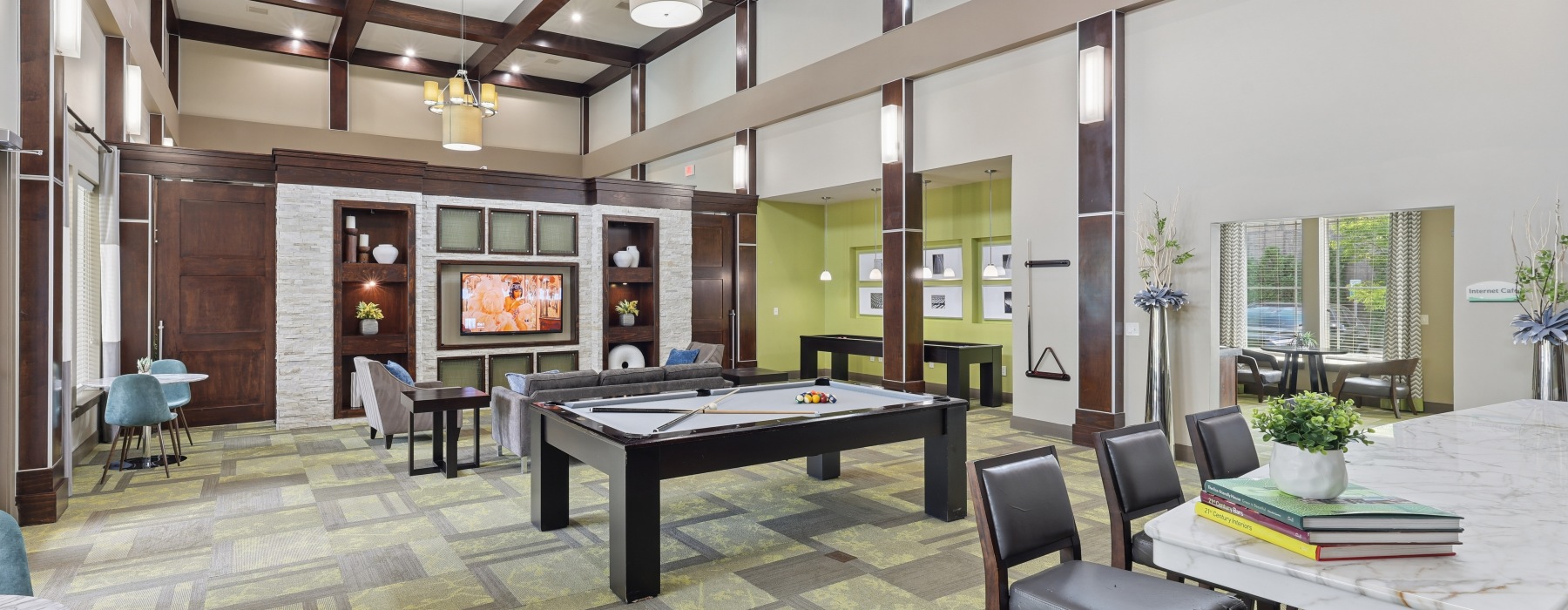 Clubhouse gathering space at Stone Pointe apartments featuring soft accent lighting, a large dining and board game table, plush seating, and warm decorative accents.