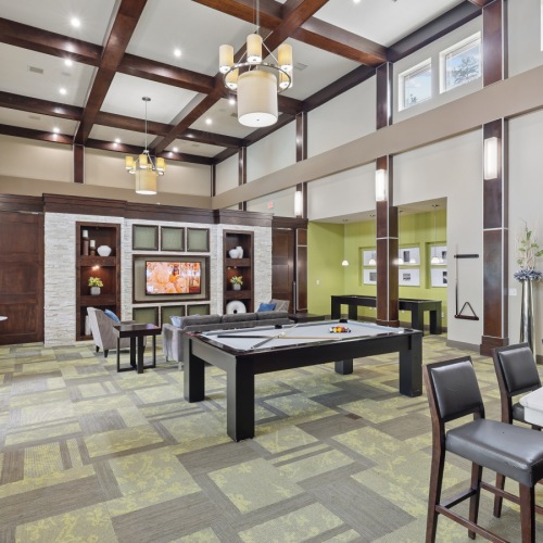 Clubhouse gathering space at Stone Pointe apartments featuring soft accent lighting, a large dining and board game table, plush seating, and warm decorative accents.